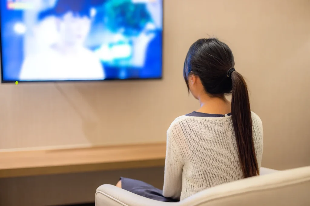 Back view of a woman sitting on a sofa watching a TV mounted on a false wall.